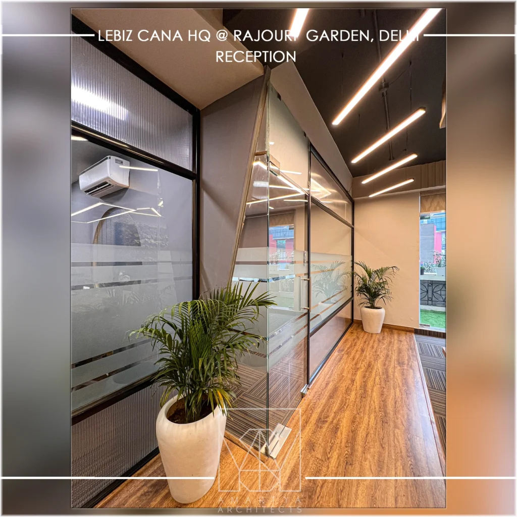 Glass partition office corridor with indoor plants, wooden flooring and modern lighting by office interior designers Amartya architects in Delhi NCR.