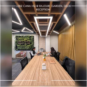 Contemporary office meeting room with long wooden table, green wall and designer lighting by interior design firms in Delhi NCR.