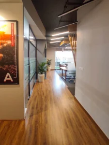Modern office corridor with glass partitions, wooden flooring and ceiling lights designed by commercial architects near me.