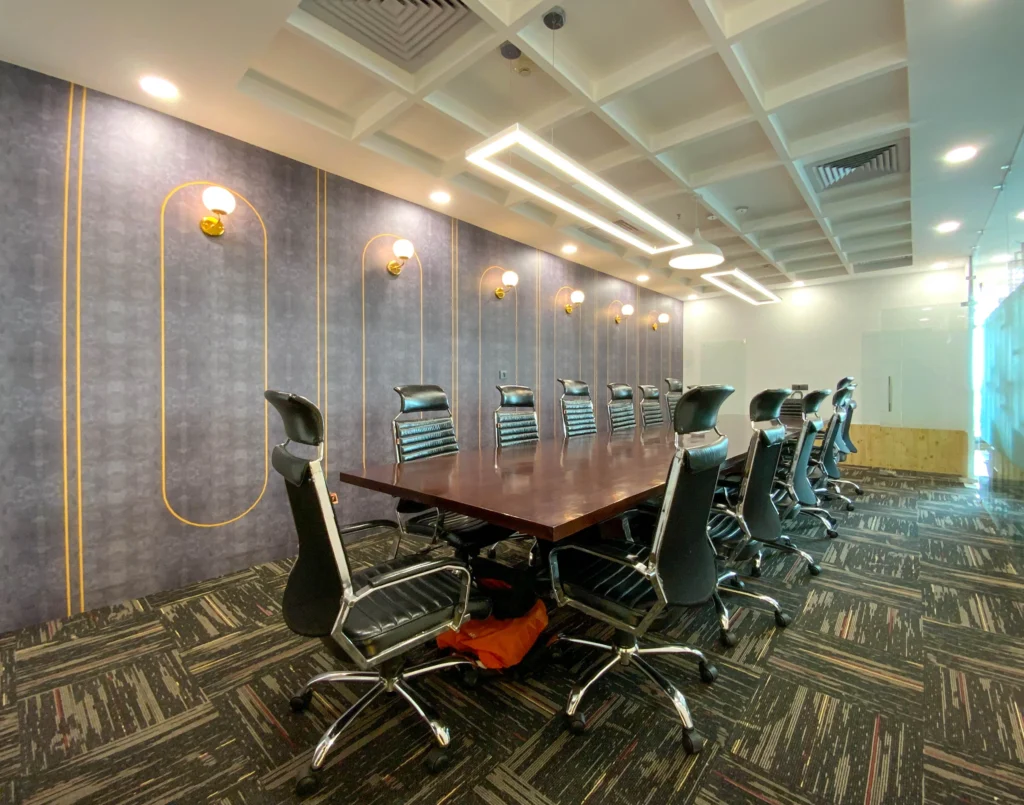 Modern corporate conference room interior with long wooden meeting table, executive chairs, decorative wall lighting and false ceiling design by Amartya Architects