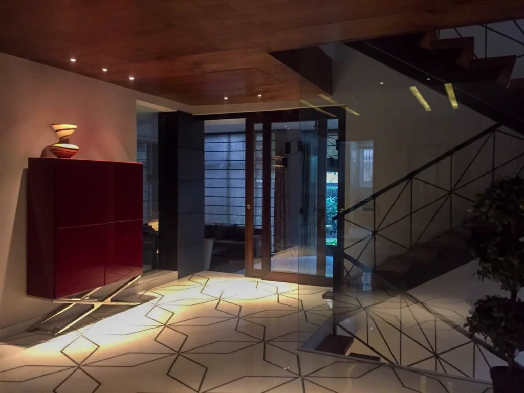 Premium home interior with double-height foyer, glass partitions, wooden ceiling panels and designer staircase, showcasing architectural and interior design services by interior architects near me.