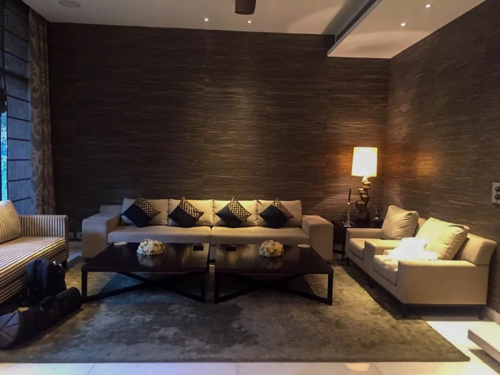 uxury living room interior with textured dark wall finish, plush sofas, designer coffee tables and soft lighting, showcasing modern interior design by top interior designers near me in Delhi.