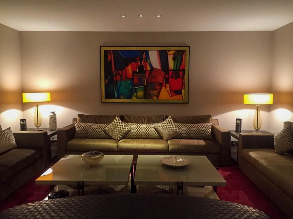 Elegant living room interior design with symmetrical sofa seating, warm ambient lighting, glass coffee table and curated wall art, designed by a professional interior designer near me offering residential interior design services in Delhi NCR.