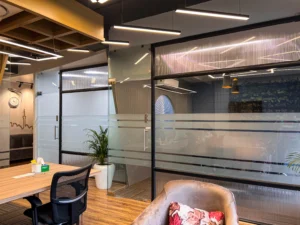 Glass partition office interior with modern lighting, wooden flooring and seating designed by commercial interior architects in Delhi