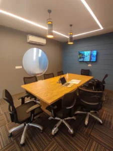 Modern office meeting room with wooden conference table, ergonomic chairs, pendant lights and circular glass detail designed by Amartya architect a commercial interior designers in Delhi NCR.