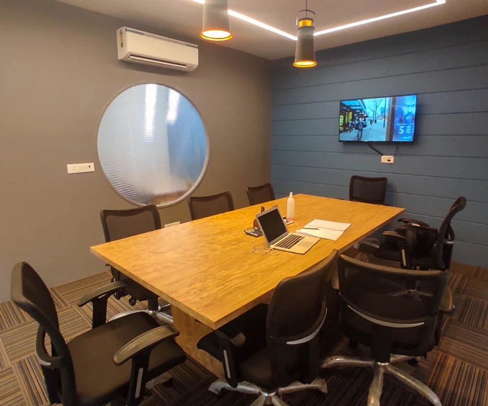 Modern office meeting room with wooden conference table, ergonomic chairs, pendant lights and circular glass detail designed by Amartya architect a commercial interior designers in Delhi NCR.