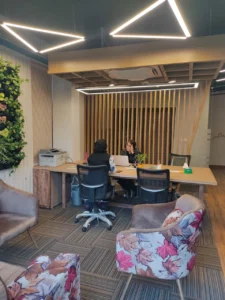 Contemporary office workspace with wooden workstations, indoor green wall, geometric LED ceiling lights and collaborative seating designed by Amartya architects a commercial interior designers in Delhi NCR.