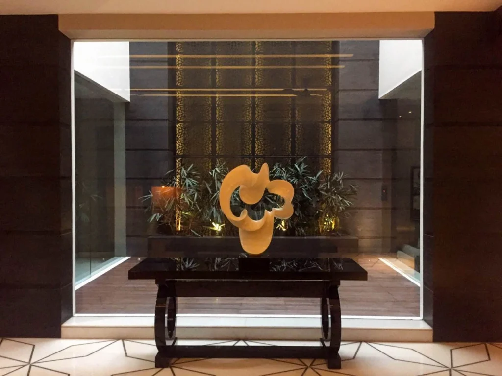 Contemporary home courtyard interior with decorative sculpture, indoor landscaping and glass enclosure, blending architecture and interior design by a Delhi based interior design firm.