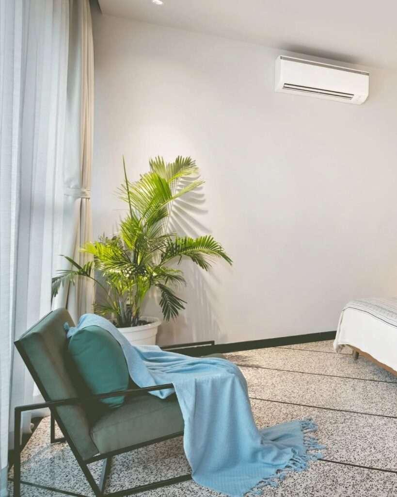 Minimal bedroom corner with lounge chair, indoor plant, soft curtains, and terrazzo flooring designed by expert bathroom interior designers with a clean and calming modern aesthetic.